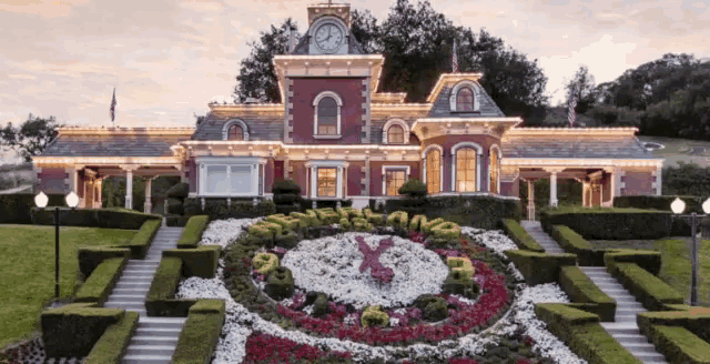 a large house with a clock on top of it and flowers in front of it