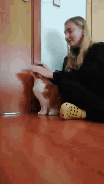 a woman is petting a cat on the floor while wearing yellow crocs .