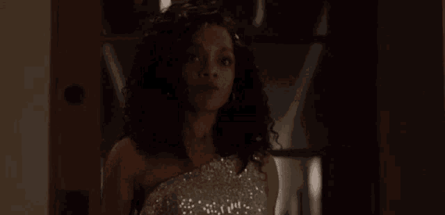 a woman in a sparkly dress is standing in a dark room looking at the camera .