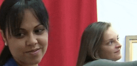 two women are standing in front of a red curtain and one is smiling