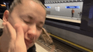 a woman sitting at a train station with her eyes closed and her hands on her face