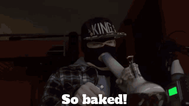 a man wearing a mask and a hat that says king smoking a bong