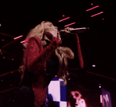 a woman singing into a microphone with a man behind her