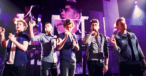 a group of men singing on a stage in front of a screen that says one direction