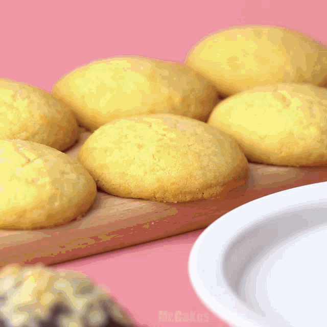 a bunch of yellow cookies on a wooden cutting board next to a white plate that says mr. cakes