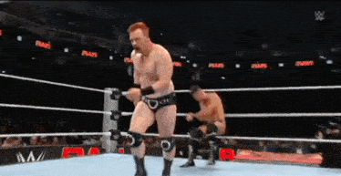 two men are wrestling in a wrestling ring and one of them is wearing shorts .