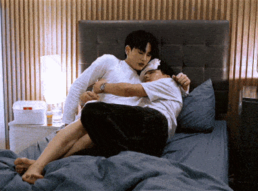 two men are hugging each other on a bed and one has a bandaged head