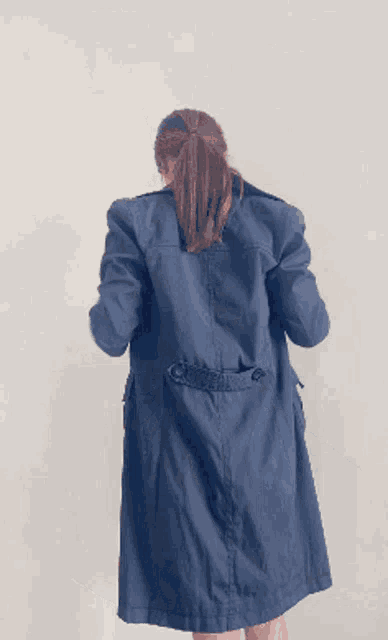 a woman in a black coat and shorts is dancing in front of a white wall