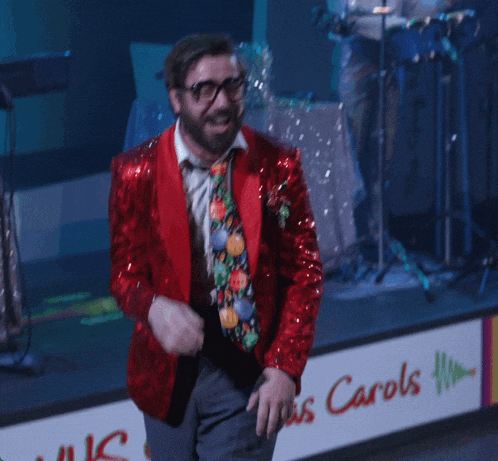 a man in a red jacket stands in front of a sign that says ' carols '