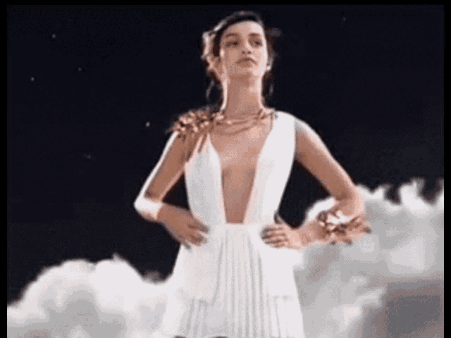 a woman in a white dress with a plunging neckline is standing in the clouds .