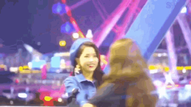 two women are hugging in front of a ferris wheel at night .
