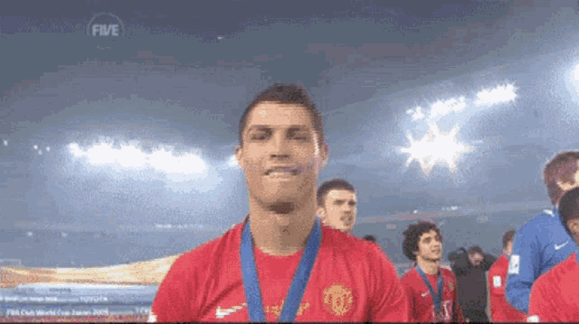 a man in a red shirt with a medal around his neck stands in front of a screen that says fifa