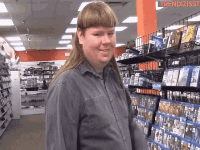 a man with a mullet is standing in front of a shelf of dvds
