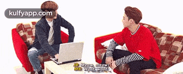 two men are sitting on a couch talking to each other and one is using a laptop .
