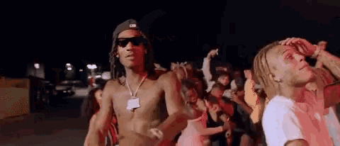 a shirtless man is dancing in front of a crowd of people at a party .
