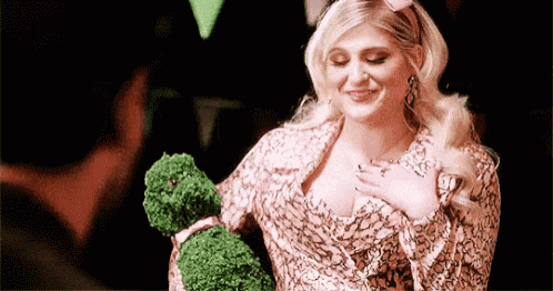 a woman in a pink dress is holding a green stuffed animal in her hands .