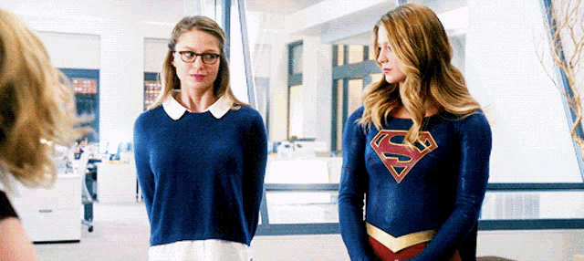 two women wearing superman costumes are standing next to each other in a room .