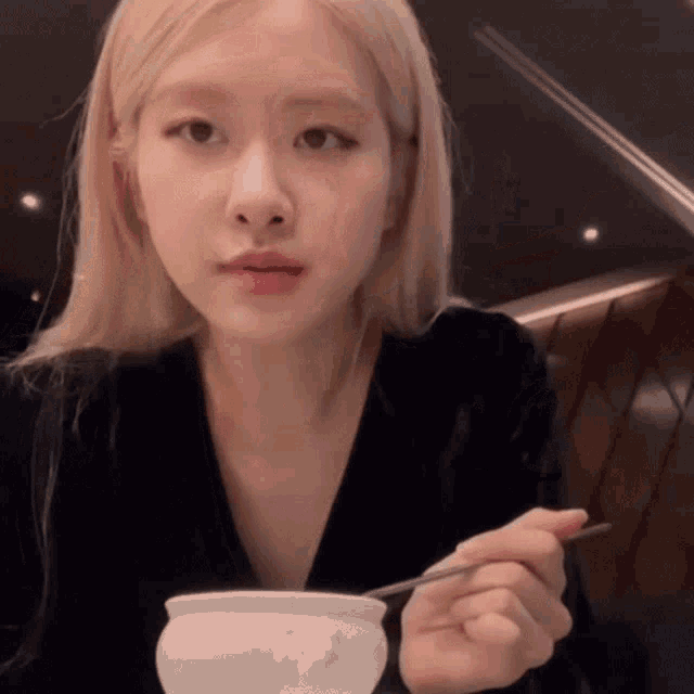 a woman is sitting at a table eating from a white bowl with chopsticks .