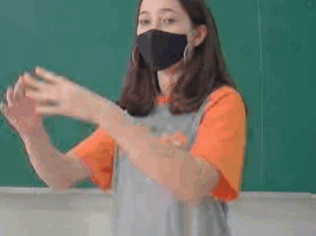 a girl wearing a mask is standing in front of a blackboard .
