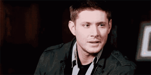 a man in a black jacket is sitting in a dark room .