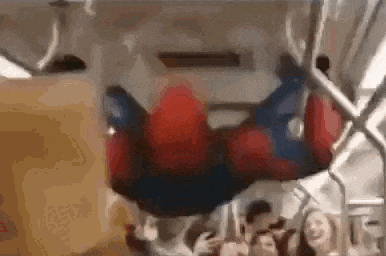 a person in a spiderman costume is hanging upside down on a subway train .