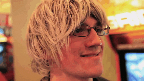 a man wearing glasses and a wig smiles in front of a sign that says ' spin '