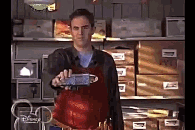 a man in an apron is standing in front of a shelf holding a box .