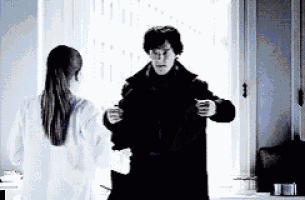 a man in a black coat is standing next to a woman in a white shirt in front of a window .