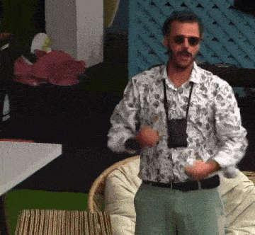a man wearing a floral shirt and sunglasses stands in front of a chair