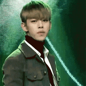 a young man wearing a jacket and tie is standing in front of a green background .