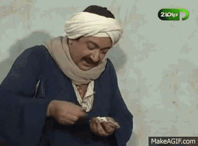 a man wearing a turban and a scarf is holding a piece of paper in his hands .