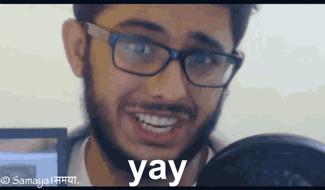 a man with glasses and a beard is smiling and says yay