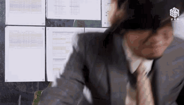 a man in a suit and tie is sitting at a desk in front of a wall with papers on it .