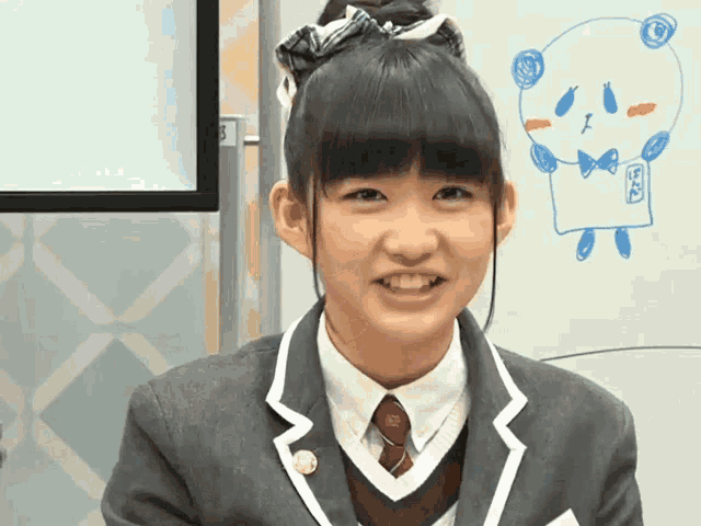 a girl in a school uniform is smiling in front of a whiteboard with a drawing of a bear on it