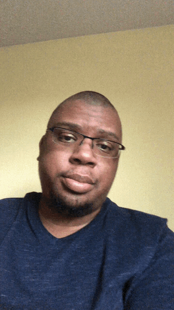 a man wearing glasses and a blue shirt makes a funny face