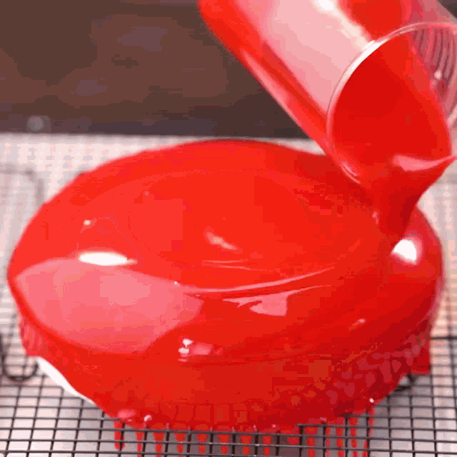 a red liquid is being poured onto a cake on a cooling rack