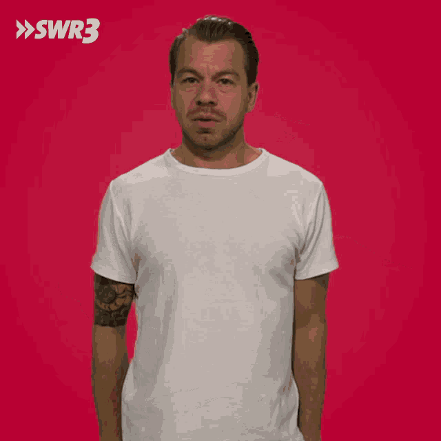 a man in a white shirt is pointing at his ear with a swr3 logo in the background