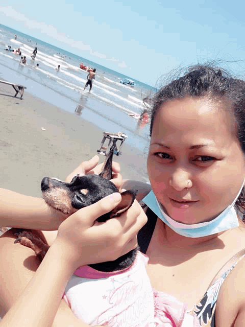 a woman wearing a mask holds a small dog in her arms