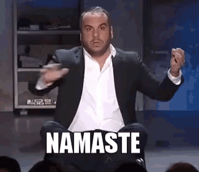 a man in a suit is sitting in a lotus position in front of a crowd and saying namaste .