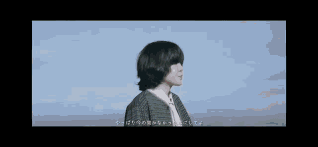 a man with short hair is standing in front of a body of water with a blue sky in the background .