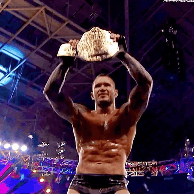 a shirtless wrestler is holding a wrestling championship belt over his head