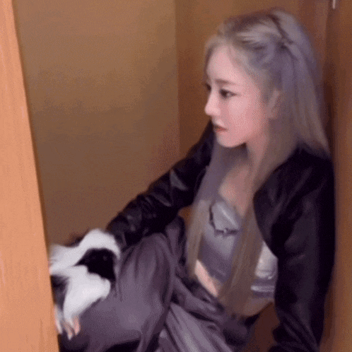 a woman with long purple hair is sitting in a closet holding a cat .