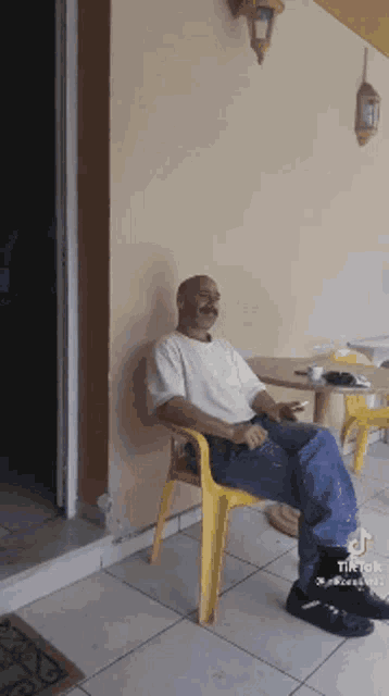 a man is sitting in a yellow chair smoking a cigarette .