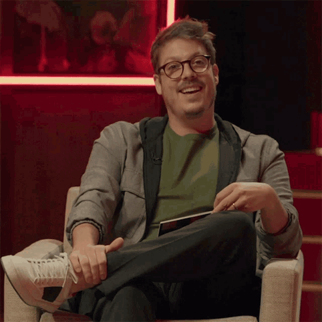 a man wearing glasses is sitting in a chair with his feet crossed