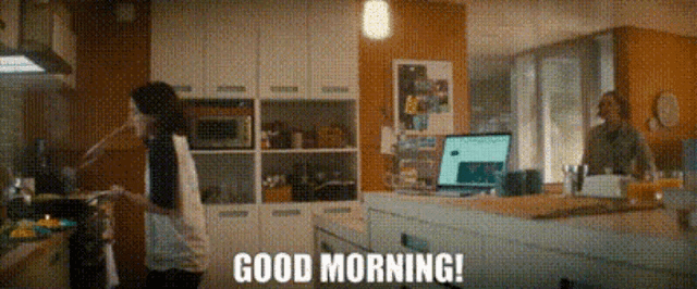 a man and a woman are standing in a kitchen with the words good morning written on the screen .