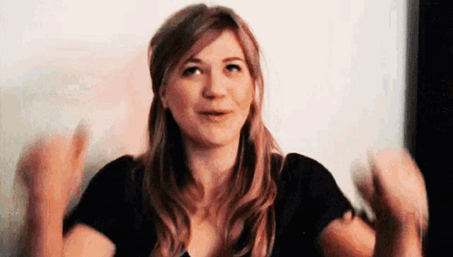 a woman in a black shirt is making a funny face while holding her hands up in the air .