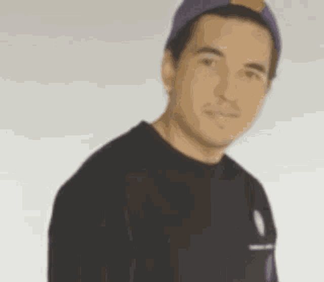 a man wearing a purple hat and a black shirt is standing in front of a white background .
