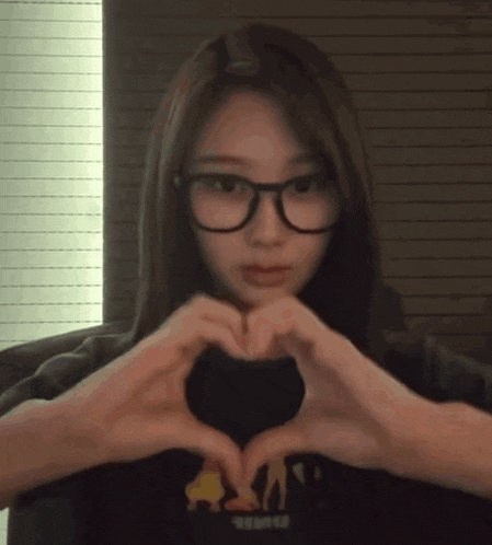 a girl wearing glasses makes a heart shape with her hands