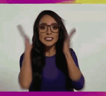 a woman wearing glasses and a purple shirt is clapping her hands .