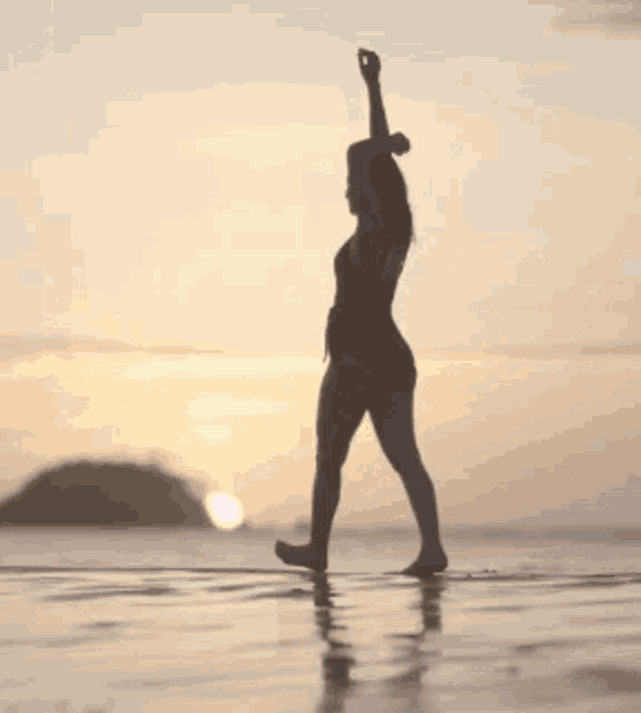 a silhouette of a woman walking on the beach